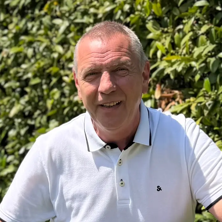 Udo Meschede, lächelnd vor einer grünen Hecke.